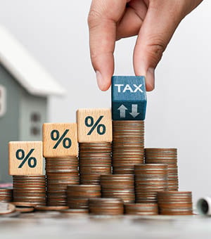 Concept of house and property tax. Interest on property, debt payment, property tax, mortgage. Stack of coins with wooden blocks with symbol of interest on house background.