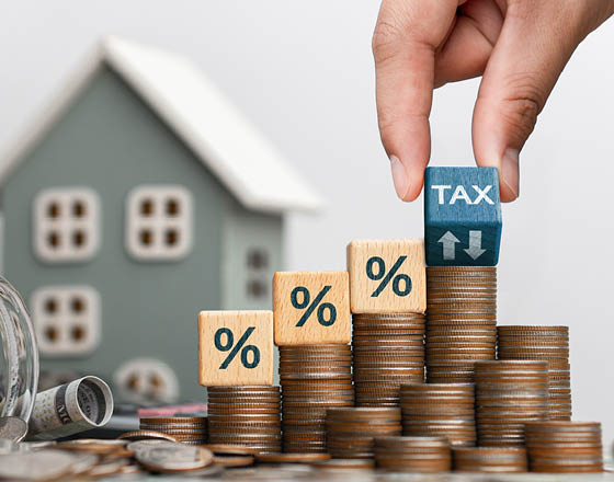 Concept of house and property tax. Interest on property, debt payment, property tax, mortgage. Stack of coins with wooden blocks with symbol of interest on house background.